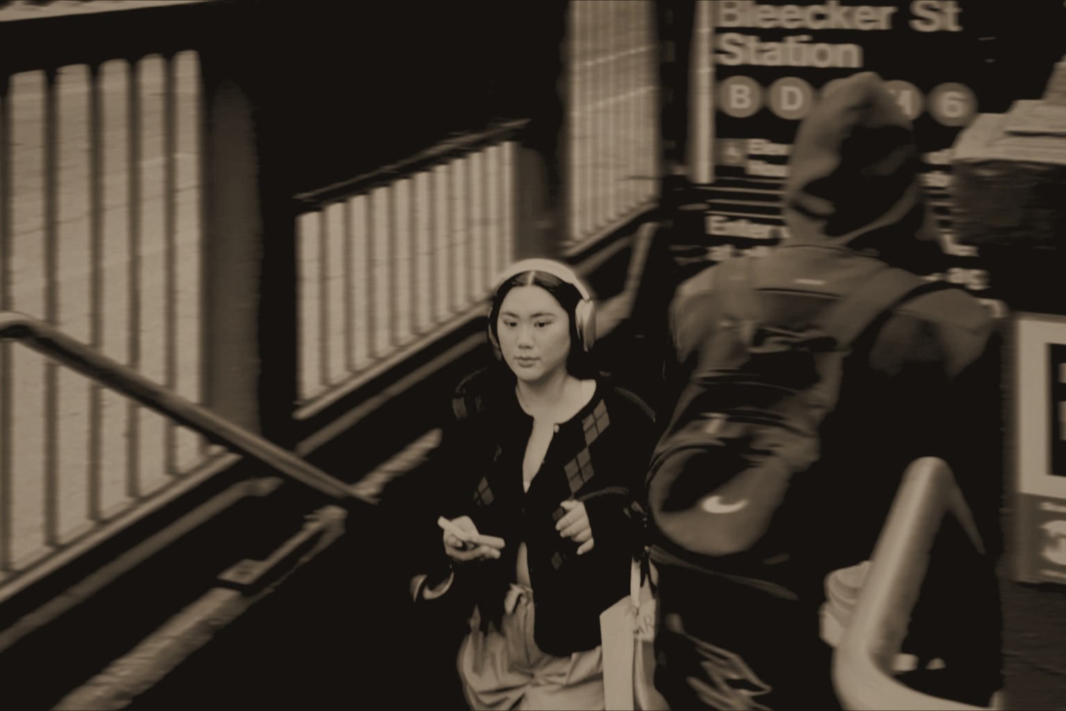 Kate K Deng emerging from the Bleecker Street subway station in a warm sepia city portrait.