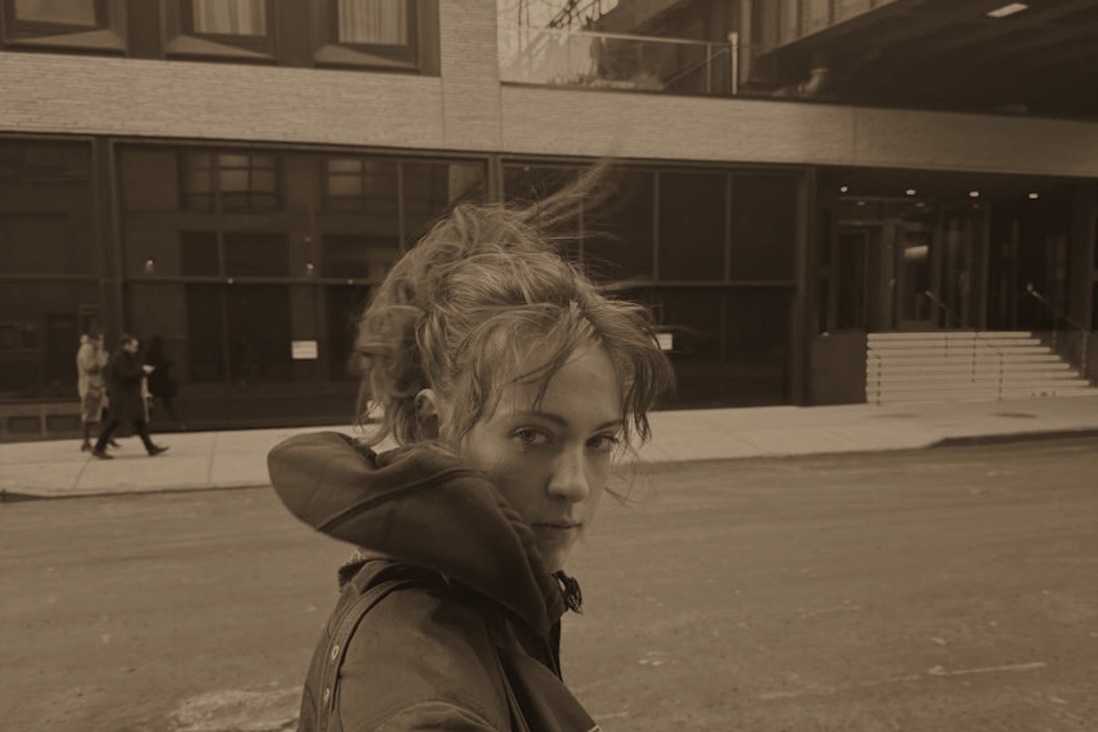 Quinn Dowd in a warm brown-tinted street portrait, turning back toward the camera.